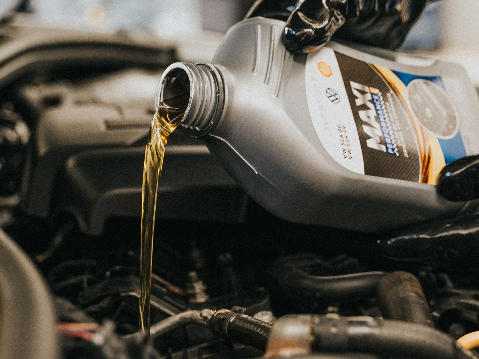 Mano con guante vierte aceite de motor nuevo desde un bidón sobre el motor de un auto