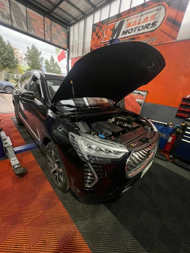 SUV Haval negro con el capó abierto sobre el piso naranja y negro del taller